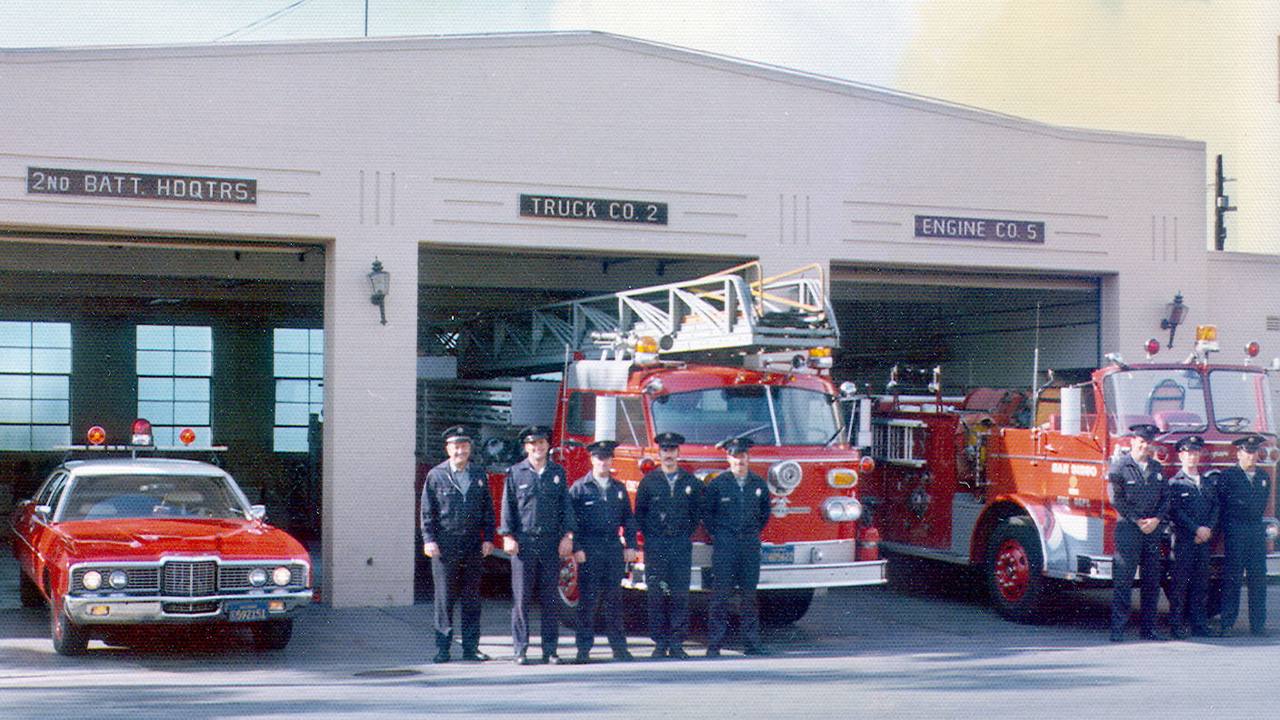 Jim Pfister and his crew standing with two engines outside a fire station.