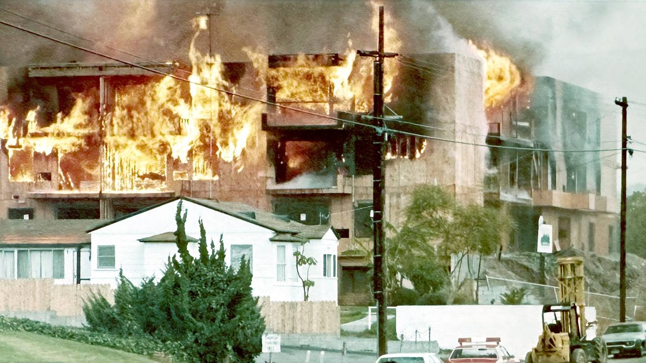An apartment building fully engulfed in flame at night.