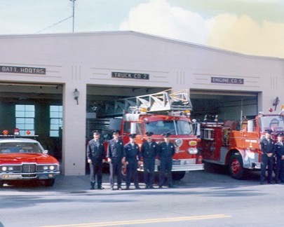 Jim Pfister and his crew standing with two engines outside a fire station.