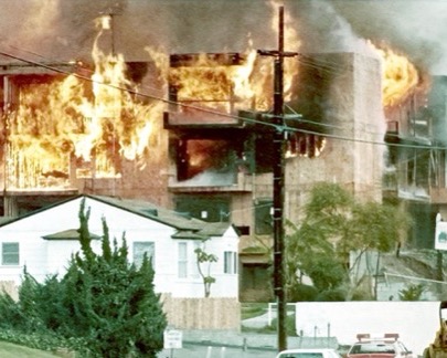 An apartment building fully engulfed in flame at night.